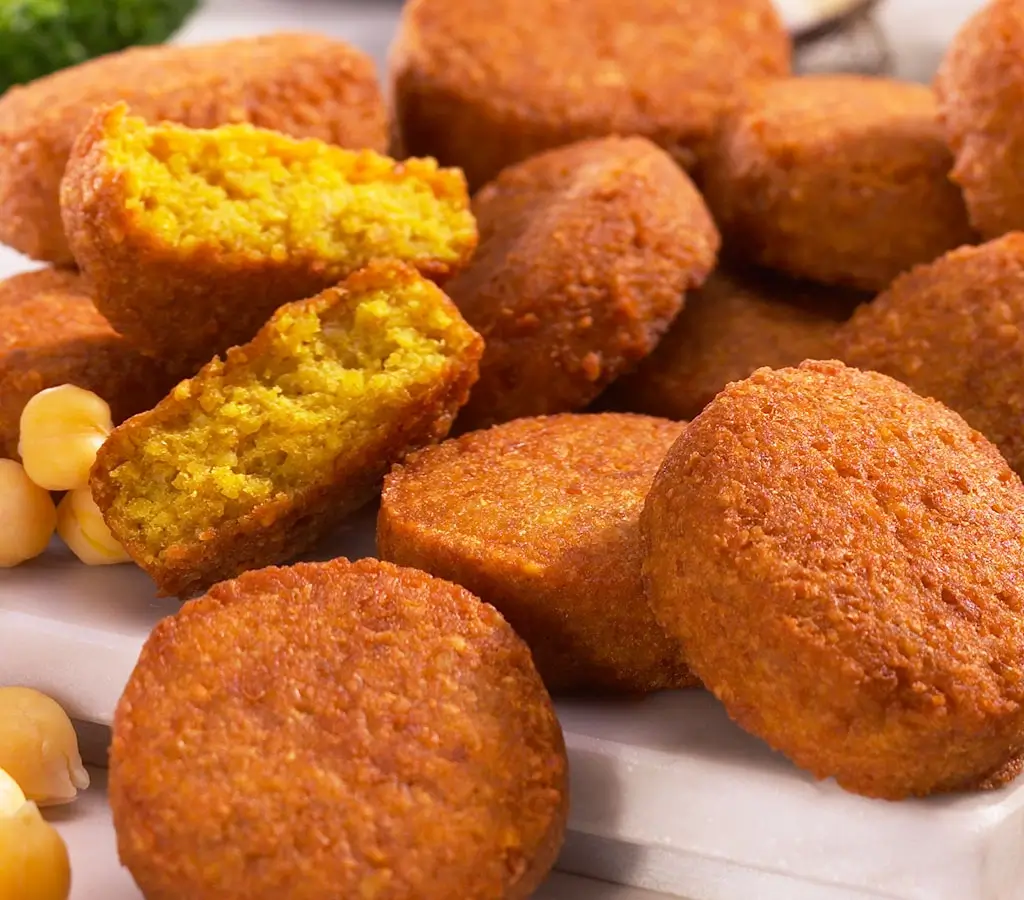 Mehrere goldbraune, runde Falafel mit einer geöffneten, gelben Innenansicht